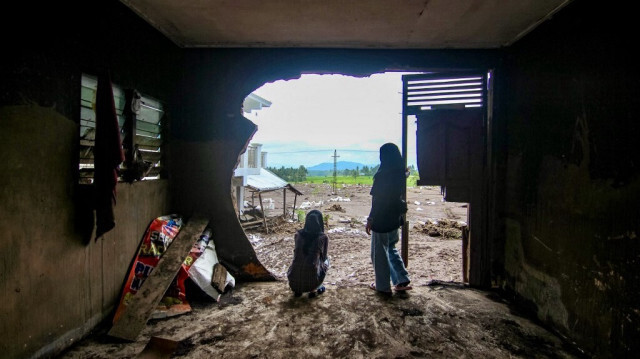 Deux femmes observent les conséquences d'une crue soudaine à travers un trou dans le mur d'une maison du village de Limo Kaum, à Tanah Datar, Sumatra Ouest, le 15 mai 2024.