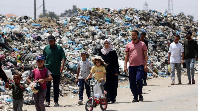 Une jeune fille fait du vélo alors que des gens passent devant des ordures entassées près de tentes montées par des Palestiniens déplacés à Khan Yunis, dans le sud de la bande de Gaza, le 18 mai 202.