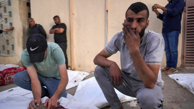 Un Palestinien réagissant tandis qu'un autre tient la main d'une personne tuée lors d'un bombardement israélien, dans la cour de l'hôpital des Martyrs d'Al-Aqsa à Deir al-Balah, dans le centre de la bande de Gaza, le 11 mai 2024, dans le cadre du conflit actuel entre Israël et le mouvement palestinien Hamas.