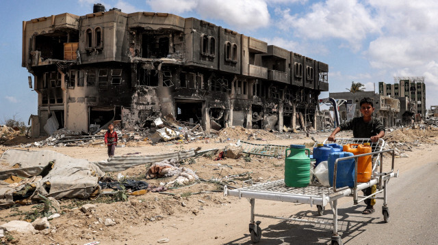Un garçon poussant un lit d'hôpital utilisé comme chariot de fortune pour transporter des jerrycans d'eau le long d'une rue devant un bâtiment incendié à Khan Yunis dans le sud de la bande de Gaza le 14 mai 2024 dans le cadre du conflit en cours dans le territoire palestinien entre Israël et le Hamas.