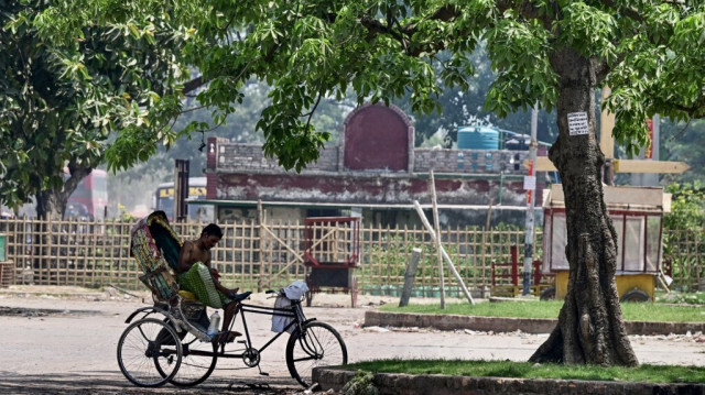 Un tireur de pousse-pousse à vélo fait une pause à l'ombre d'un arbre pour se protéger de la chaleur à Dacca, le 29 avril 2024.