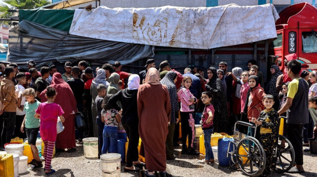 Des personnes se rassemblent avec des jerrycans pour faire le plein d'eau à partir d'un camion-citerne dans la cour d'une école de l'Office de secours et de travaux des Nations Unies pour les réfugiés de Palestine dans le Proche-Orient (UNRWA), le 14 mai 2024.