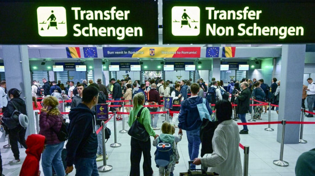 Des voyageurs marchent à côté de panneaux nouvellement installés indiquant les zones Schengen et non-Schengen quelques minutes après minuit à l'aéroport international "Henri Coanda" d'Otopeni, le 31 mars 2024.