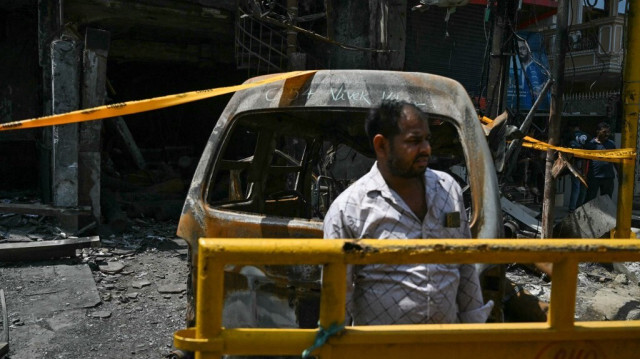 Un homme se tient près des restes d'un véhicule brûlé sur le site de l'accident, un jour après l'incendie d'un hôpital pour enfants à New Delhi, le 26 mai 2024.