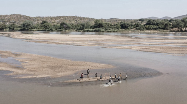 Cette vue aérienne montre un groupe de personnes, certaines portant des seaux et des filets, pataugeant le long de la rive zimbabwéenne du fleuve Limpopo (à droite), qui délimite la frontière avec l'Afrique du Sud (à gauche) à l'est de Musina, le 24 avril 2024. 