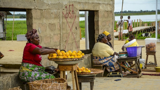 Une vendeuse vend des fruits près d'une maison marquée d'une croix rouge indiquant qu'elle sera démolie dans le cadre du projet "Ville verte de Porto-Novo" à Porto-Novo le 3 mai 2024. 