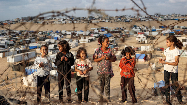 Des enfants se tenant derrière des barbelés le long d'une pente près d'un camp abritant des Palestiniens déplacés à Rafah, dans le sud de la bande de Gaza, le 30 avril 2024, dans le cadre du conflit en cours dans le territoire palestinien entre Israël et le groupe militant Hamas.