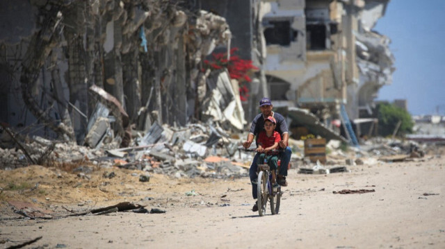 Un homme et un enfant Palestinien en vélo passent devant des bâtiments détruits en raison des bombardements de l'armée israélienne, à Khan Younes, dans le sud de la bande de Gaza, en Palestine, le 11 juin 2024.