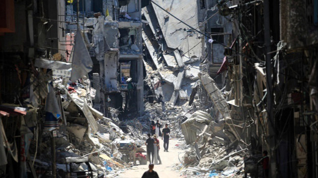 Des Palestiniens marchent dans une rue étroite devant des bâtiments détruits à Khan Younès, dans le sud de la Bande de Gaza, le 11 juin 2024.