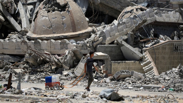 Un jeune Palestinien transportant de l'eau passe devant une mosquée détruite à Khan Yunis, dans le sud de la bande de Gaza, le 14 juin 2024.