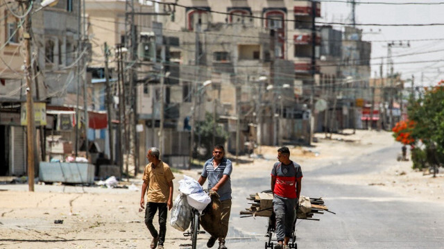 Un homme tire un chariot chargé de bois récupéré à côté d'un autre poussant un vélo chargé de sacs dans une rue de la partie est de Rafah dans le sud de la bande de Gaza le 14 juin 2024. 