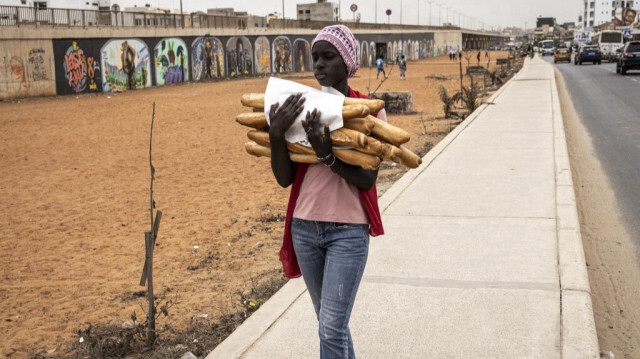 Une femme transporte des baguettes de pain le long d'une route à Dakar.