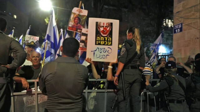 Les forces de sécurité israéliennes montent la garde alors que des manifestants brandissent des pancartes et des drapeaux nationaux lors d'une manifestation anti-gouvernementale près de la résidence du Premier ministre, Benyamin Netanyahu à Jérusalem, le 27 juin 2024.