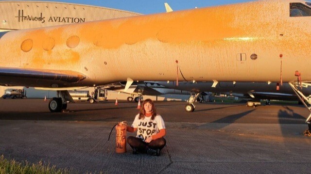 Une militante de Just Stop Oil assise devant un avion après avoir aspergé de peinture orange des jets privés à l'aéroport de Stansted, au nord-est de Londres, le 20 juin 2024.
