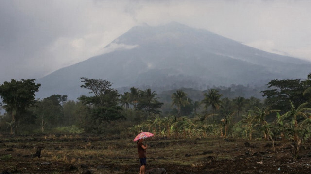 Un habitant tenant un parapluie se tient dans un terrain près de sa maison au pied du volcan du mont Kanlaon dans un village de La Castellana, province de Negros Occidental, au centre des Philippines, le 4 juin 2024, un jour après l'éruption du volcan.