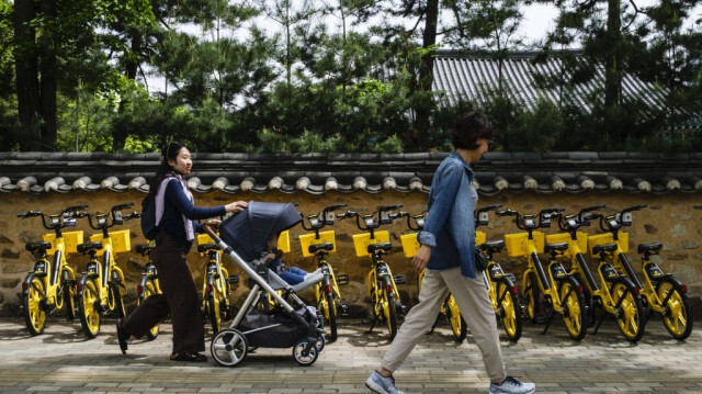 Une femme pousse son enfant dans une poussette devant des vélos de location à Séoul.