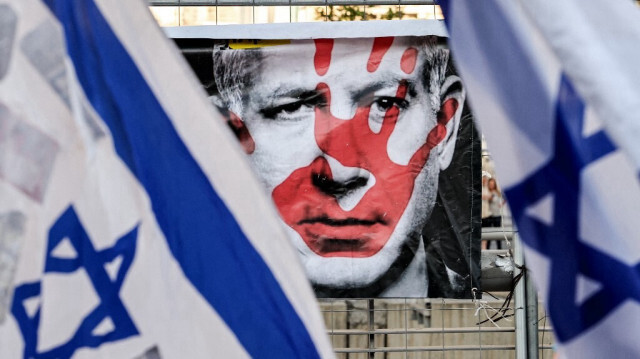 Une affiche représentant le visage du Premier ministre israélien Benyamin Netanyahu apparaît entre des drapeaux israéliens lors d'une manifestation anti-gouvernementale organisée par des militants de gauche à Tel Aviv le 6 juillet 2024.