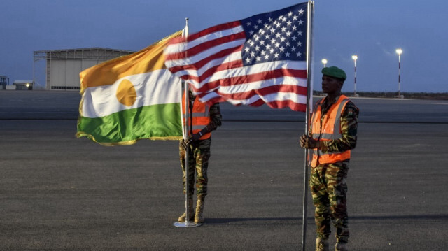 Deux soldats nigériens tiennent les drapeaux américain et nigérien sur la Base Aérienne 101 à Niamey le 7 juin 2024 lors de la cérémonie marquant le premier départ des troupes américaines du Niger. 