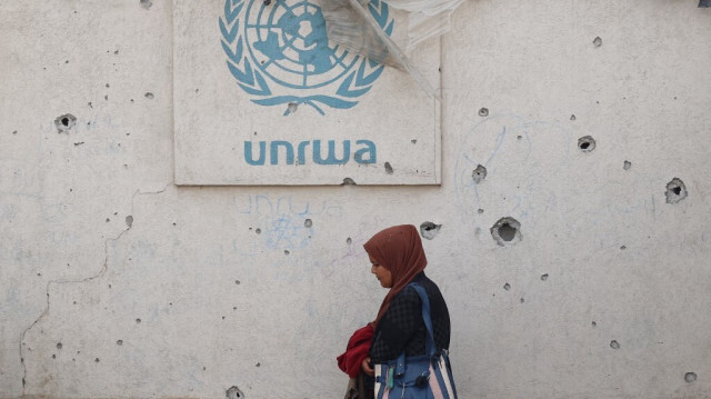 Une femme palestinienne passe devant un mur endommagé portant le logo de l'UNRWA dans un camp de personnes déplacées internes à Rafah, dans le sud de la bande de Gaza, le 28 mai 2024.