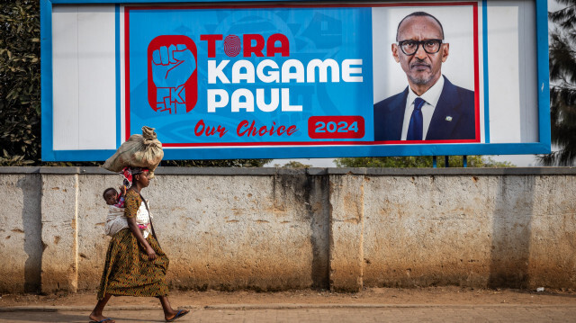 Une femme portant son bébé sur le dos passe devant un panneau électoral demandant de voter pour le président sortant du Rwanda et le candidat présidentiel du Front patriotique rwandais (FPR) Paul Kagame à Kigali, le 11 juillet 2024, avant les élections générales rwandaises de 2024.