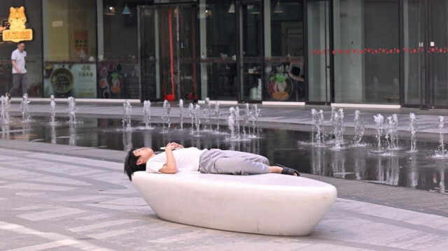 Un homme fait une sieste près d'une fontaine dans un centre commercial à Pékin, le 18 juillet 2024.