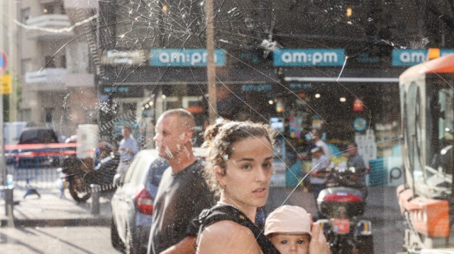 Une femme portant un bébé devant des éclats de verre après une explosion provoquée par une attaque houthie à Tel Aviv le 19 juillet 2024. 