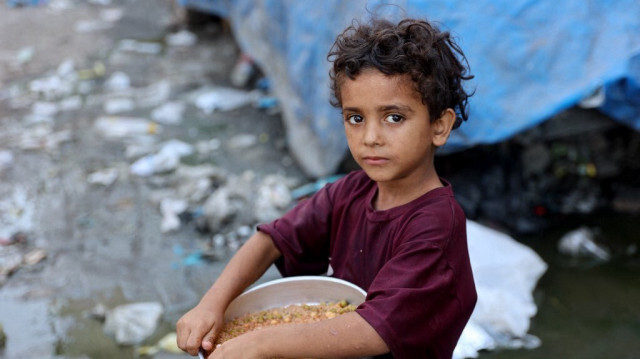 Une petite fille palestinienne déplacée de force en raison des bombardements israéliens porte un récipient contenant de la nourriture à un point de distribution, mis en place par des jeunes hommes de la famille Madhoun à Beit Lahia, dans le nord de la bande de Gaza, en Palestine, le 18 juillet 2024.