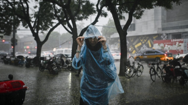 Une femme portant un imperméable marche sous une pluie battante à Pékin le 12 juillet 2024.