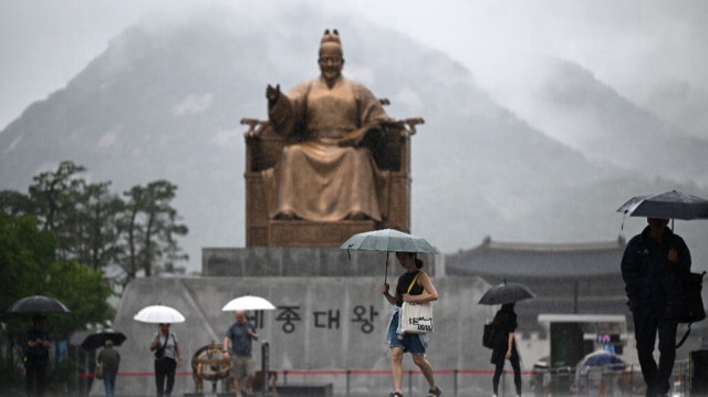 Des personnes tiennent des parapluies alors qu'elles passent devant une statue du roi Sejong sur la place centrale Gwanghwamun pendant la pluie à Séoul le 18 juillet 2024.