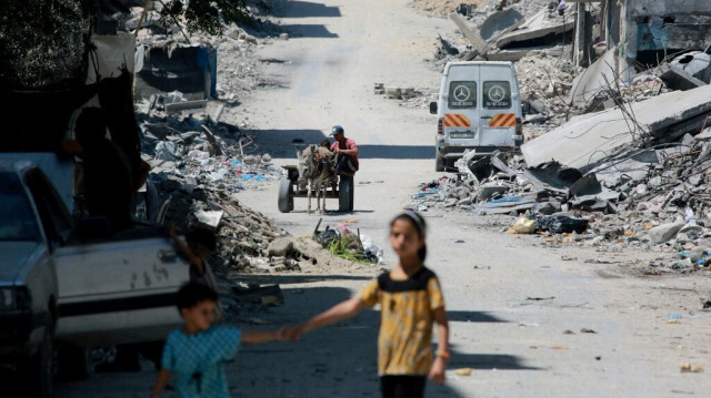 Une fille palestinienne tient la main d'un garçon alors qu'ils marchent dans une rue devant des bâtiments détruits lors de précédents bombardements israéliens, à Khan Yunis, dans le sud de la bande de Gaza, le 19 juillet 2024.