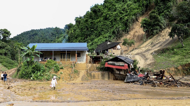 Des personnes marchent dans la boue devant les débris de biens endommagés à la suite d'un glissement de terrain provoqué par de fortes pluies dans la province de Dien Bien au Vietnam, le 25 juillet 2024.