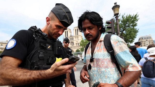 Un gendarme français inspecte le QR code d'un piéton sur son smartphone à l'entrée de la zone sécurisée établie le long de la Seine à Paris, le 18 juillet 2024.