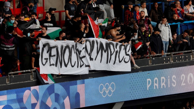 Des supporters brandissent une banderole portant l'inscription "Jeux olympiques du génocide" et agitent des drapeaux palestiniens lors du match de football du groupe D masculin entre Israël et le Paraguay pendant les Jeux olympiques de Paris 2024 au Parc des Princes à Paris, le 27 juillet 2024.