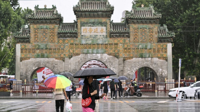 Des personnes traversant une route utilisent des parapluies pour s'abriter de la pluie à Pékin, le 30 juillet 2024.