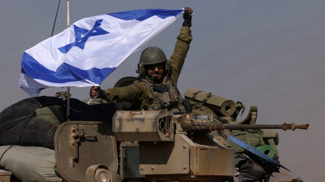 Un soldat israélien à bord d'un véhicule blindé de transport de troupes (VBTP) brandissant un drapeau israélien, près de la frontière de la bande de Gaza, le 31 décembre 2023.