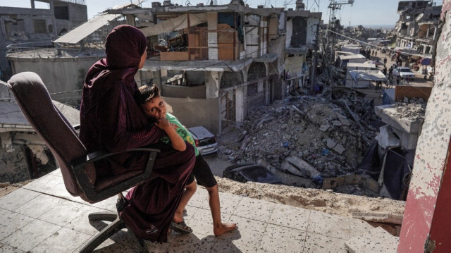 Une femme palestinienne, membre de la famille d'Ibrahim Abu Alya, assise avec un enfant palestinien sur le balcon de sa maison gravement endommagée par les bombardements israéliens, dans la ville de Bani Suheila près de Khan Yunis dans le sud de la bande de Gaza, en Palestine, le 17 juillet 2024.