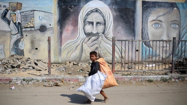 Un enfant palestinien déplacé porte des sacs alors qu'il passe devant des peintures murales à Deir el-Balah, dans le centre de la bande de Gaza, le 7 juillet 2024.
