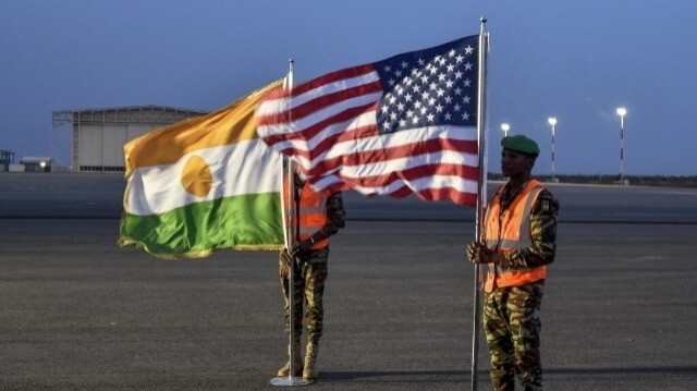 Deux soldats nigériens tiennent les drapeaux américain et nigérien sur la base aérienne 101 à Niamey, le 7 juin 2024, lors de la cérémonie du premier départ des troupes américaines du Niger. 