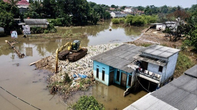 Une pelleteuse dégageant l'eau en ramassant les ordures à côté des maisons des résidents qui ont été submergées par l'eau après l'inondation d'une rivière à la suite d'un glissement de terrain d'un tas d'ordures qui a bloqué son cours d'eau à Depok.