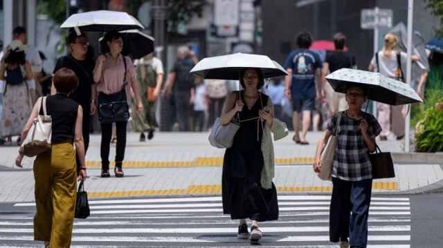 Des piétons avec des parasols marchent sur un trottoir par temps chaud dans le centre de Tokyo le 9 juillet 2024.