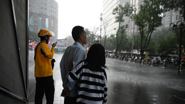 Des personnes attendent à l'extérieur d'un centre commercial pendant une averse à Pékin, en Chine, le 31 juillet 2024.