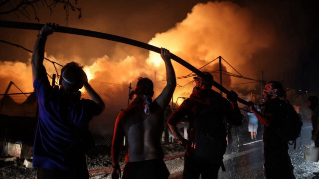 Des volontaires tiennent un tuyau d'eau pour aider les pompiers à éteindre un incendie dans une usine de bois à Vrilissia, en périphérie d'Athènes, le 12 août 2024. 