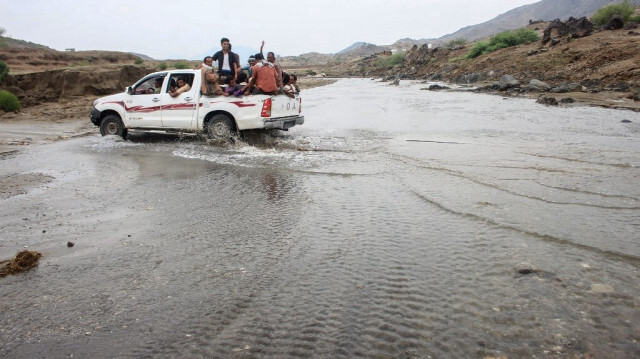 Des hommes circulant à l'arrière d'une camionnette sur une route inondée après de fortes pluies dans la région d'Abs au Yémen, le 09 août 2024.