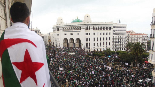 Un Algérien drapé dans le drapeau national observe les manifestants se rassembler pour protester contre le président malade Abdelaziz Bouteflika devant La Grande Poste, au centre d'Alger, le 22 mars 2019.