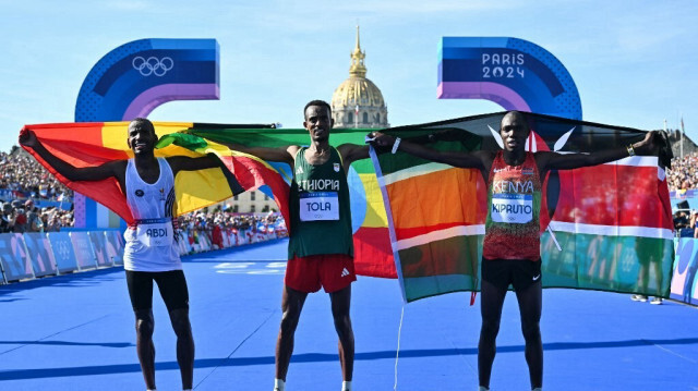 Le vainqueur éthiopien Tamirat Tola (C), le deuxième belge Bashir Abdi (G) et le troisième kenyan Benson Kipruto célèbrant après le marathon masculin de l'épreuve d'athlétisme des Jeux Olympiques de Paris 2024 aux Invalides à Paris, le 10 août 2024. 