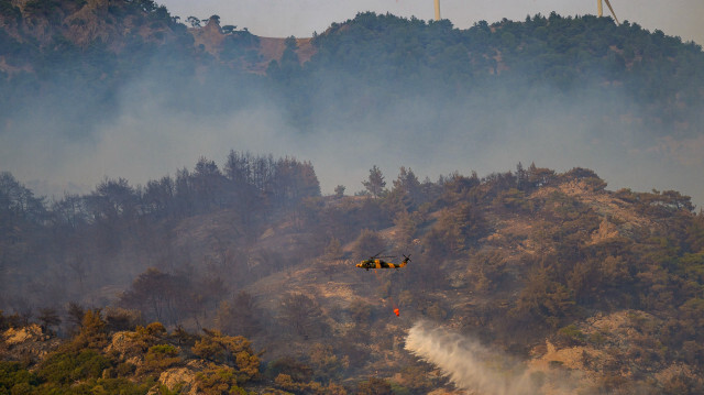 Cette photo montre un hélicoptère en train d'arroser un feu de forêt dans la province occidentale d'Izmir, en Türkiye, le 17 août 2024. Les pompiers luttent contre un violent incendie de forêt dans la station balnéaire égéenne d'Izmir pour la troisième journée, le 17 août 2024. Des centaines de personnes ont été évacuées pendant la nuit.