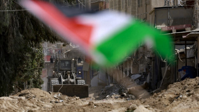 Un bulldozer de l'armée israélienne détruit une route dans le camp de réfugiés de Nur Shams à Tulkarem, avec un drapeau palestinien flottant au premier plan, le 29 août 2024.