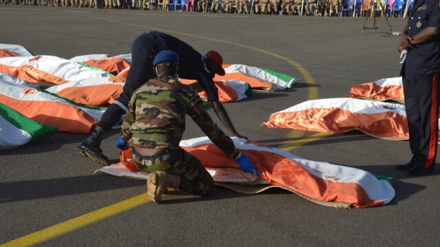 Des militaires nigériens couvrent les corps des militaires avec le drapeau national du Niger à la base aérienne de Niamey, le 13 décembre 2019. 