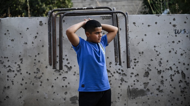 Un jeune Palestinien se tient devant un mur criblé de balles et d'éclats d'obus dans la petite ville de Zababdeh, au sud-est de Jénine, en Cisjordanie occupée, le 30 août 2024, à la suite d'un raid de l'armée israélienne.