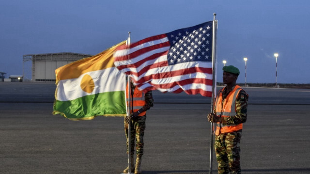 Deux soldats nigériens tiennent les drapeaux américain et nigérien sur la base aérienne 101 à Niamey, le 7 juin 2024, lors de la cérémonie du premier départ des troupes américaines du Niger. 